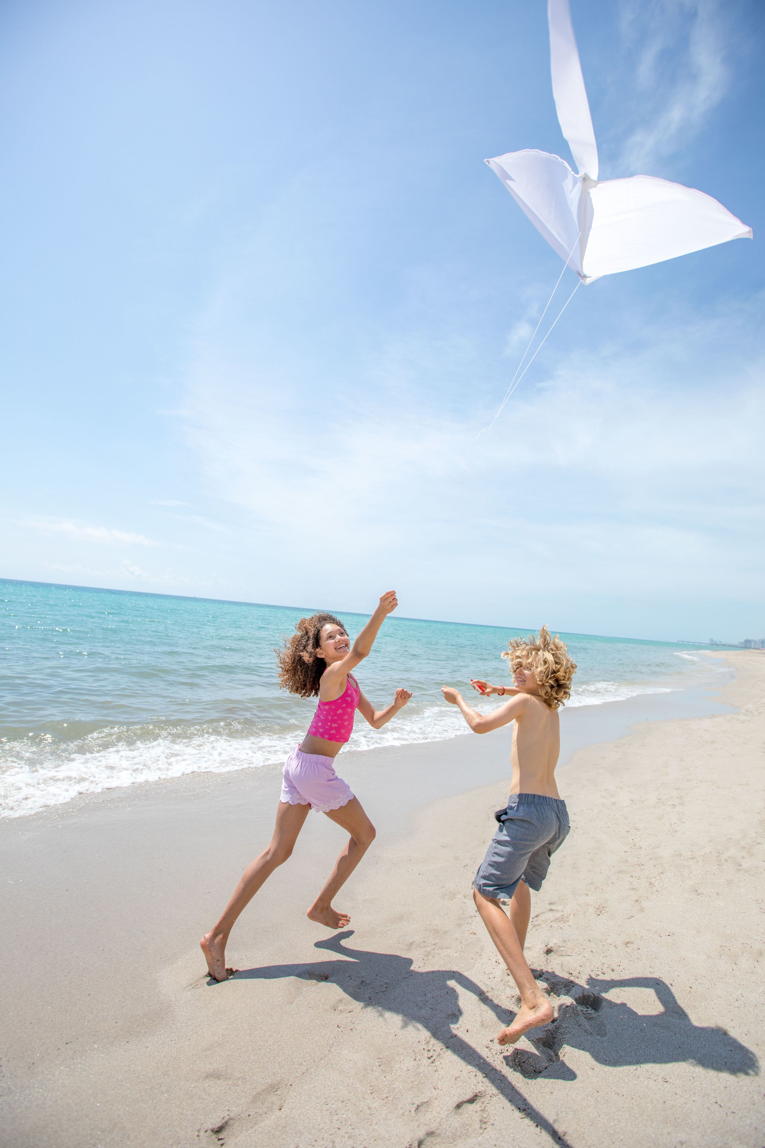 Two children playing with a kite on a sandy beach with the ocean in the background.