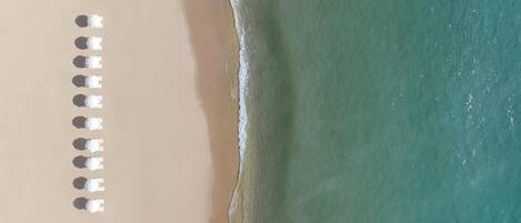 An aerial view of a beach with rows of white umbrellas aligned along the shoreline.