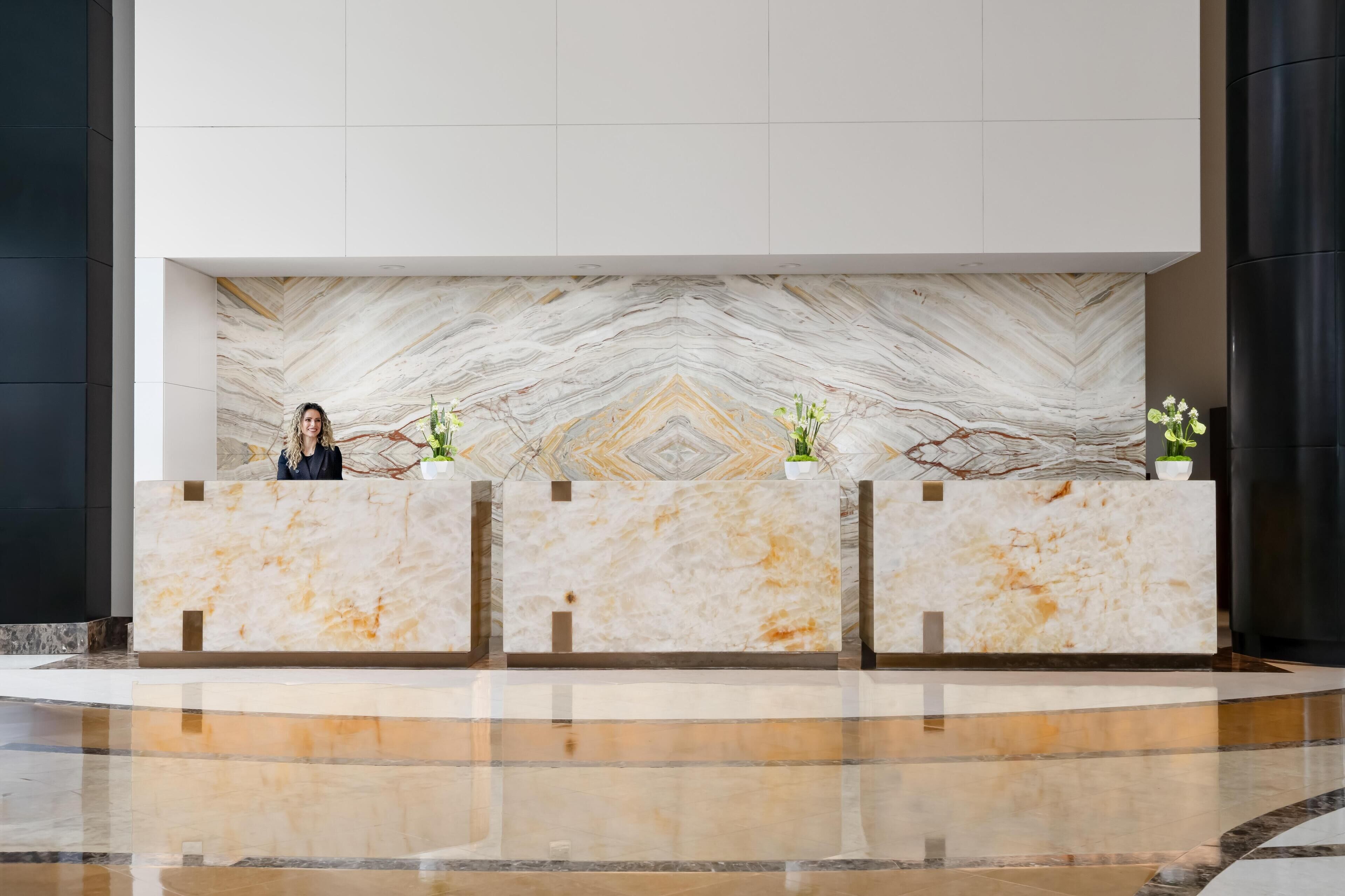 A reception desk with marble surfaces and potted plants.