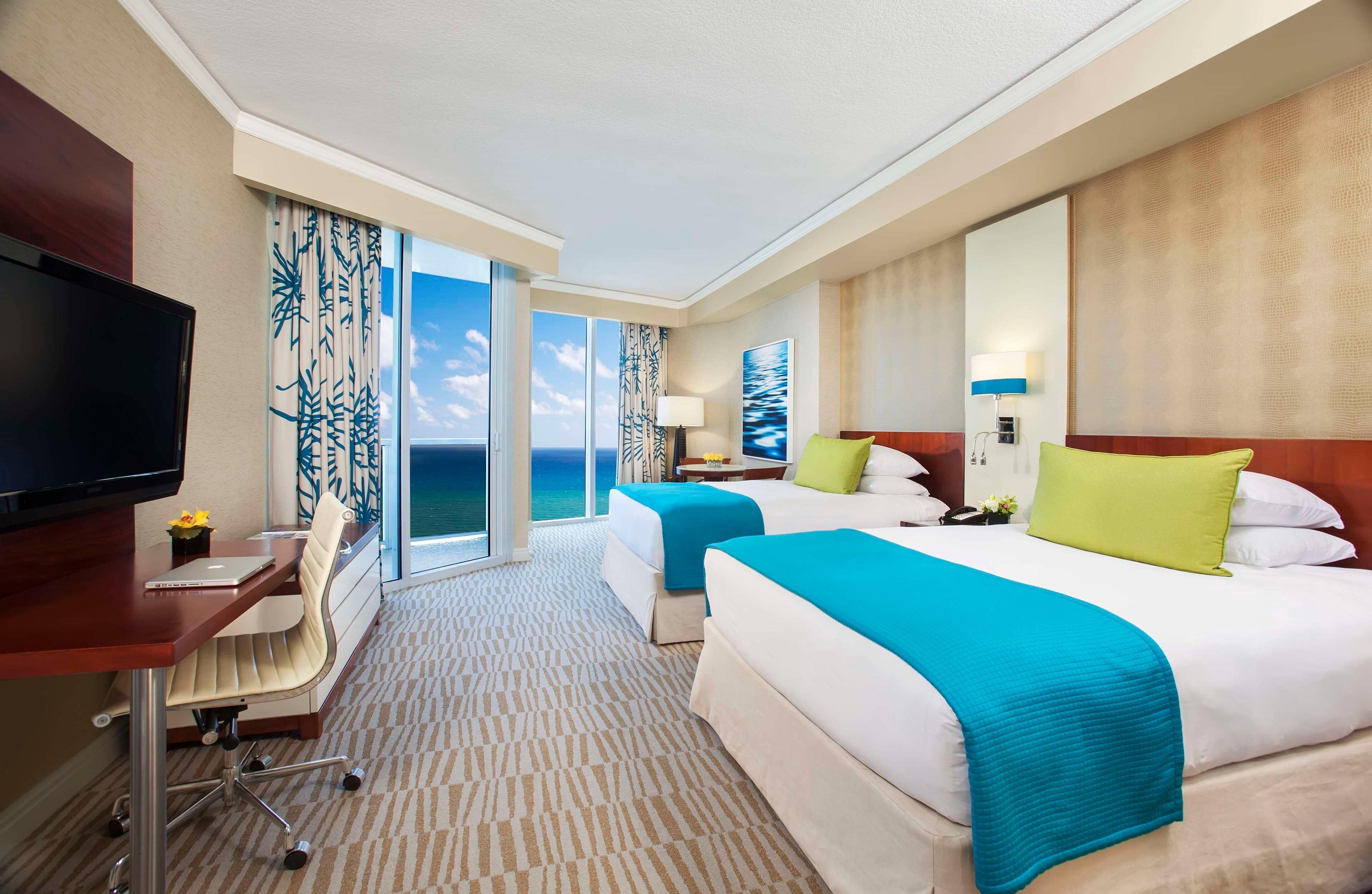 A hotel room with a large bed, a desk with a chair, a television, and a view of the ocean.