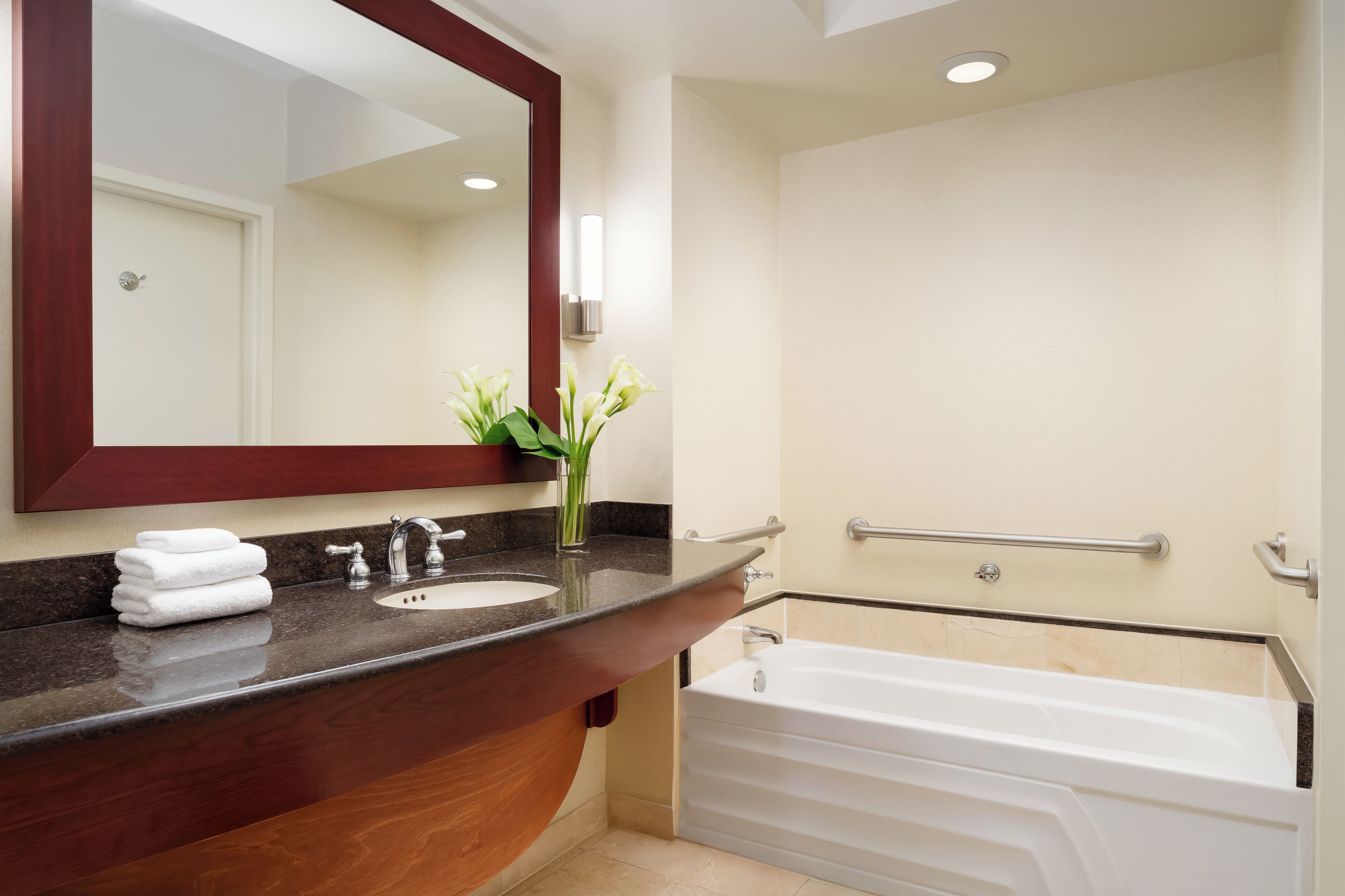Une salle de bain moderne avec un meuble-lavabo en bois, un évier, un miroir, un vase avec des fleurs et une baignoire blanche.