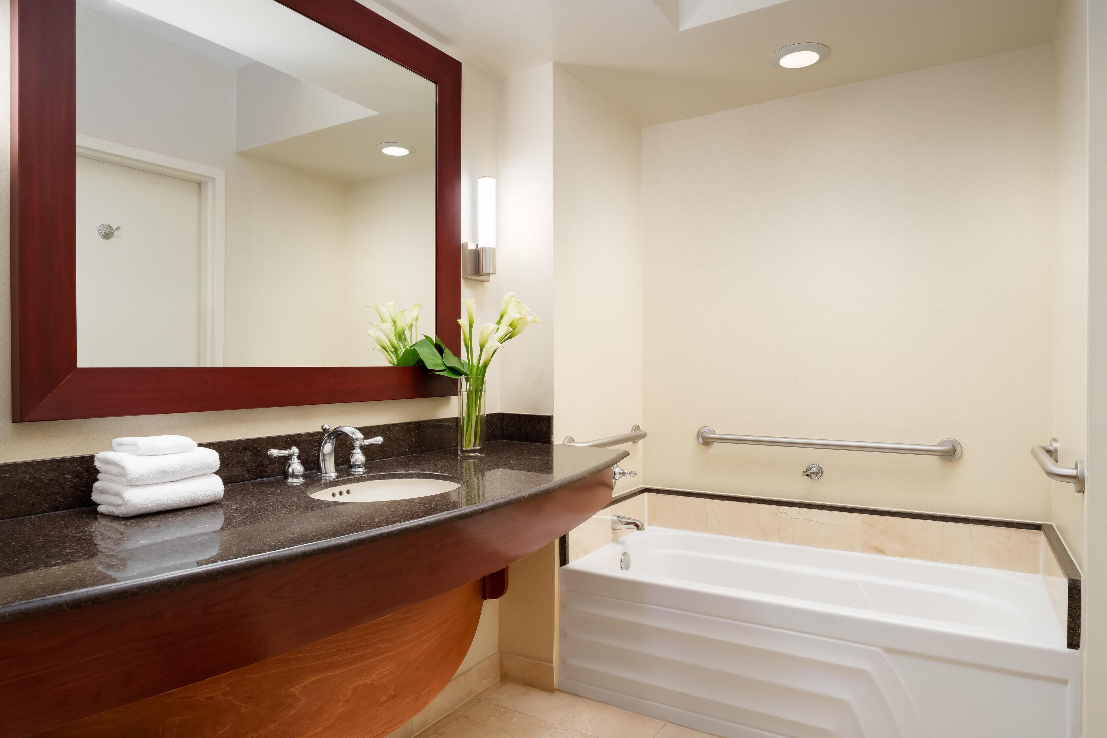 Un baño moderno con tocador de madera, lavamanos, espejo y bañera blanca.