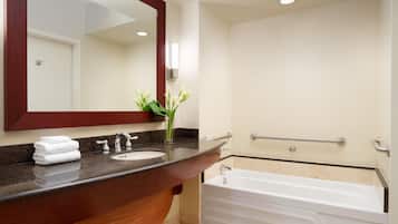 A modern bathroom with a wooden vanity, a sink, a mirror, and a white bathtub.