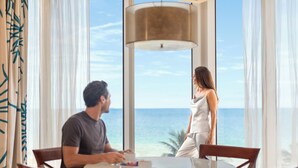 Habitació amb una finestra gran que dona al mar, una taula rodona i una làmpada moderna.