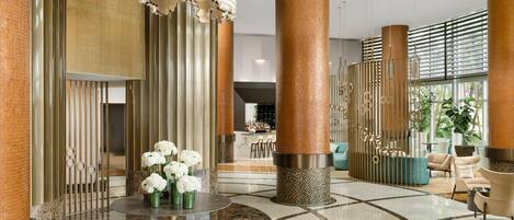 A spacious lobby with a marble floor, large columns, and a decorative light fixture.