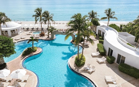 A resort pool with palm trees, lounge chairs, and a beach view.