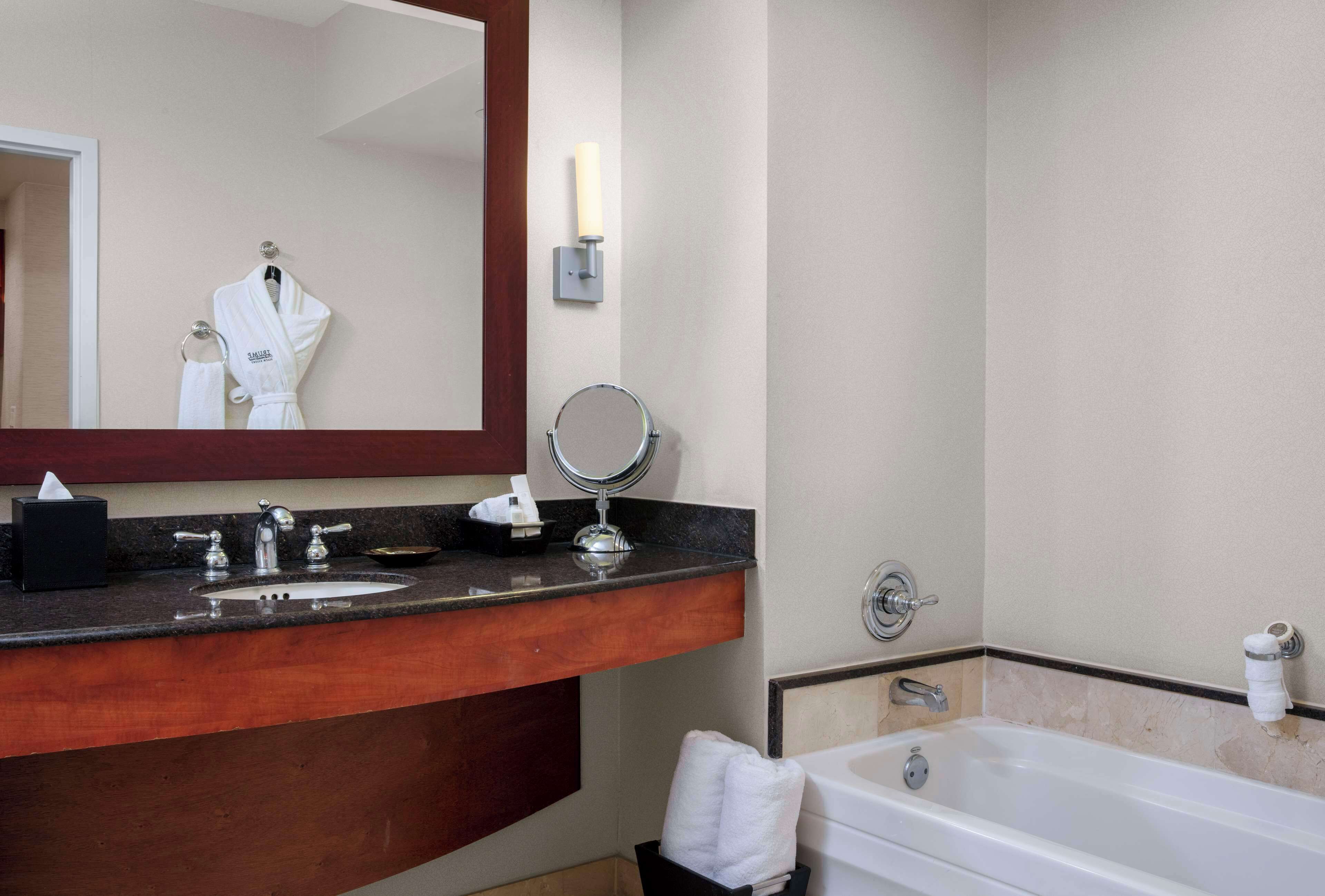 A hotel bathroom with a wooden vanity, a sink, a mirror, a round mirror, a bathtub, and a towel rack.
