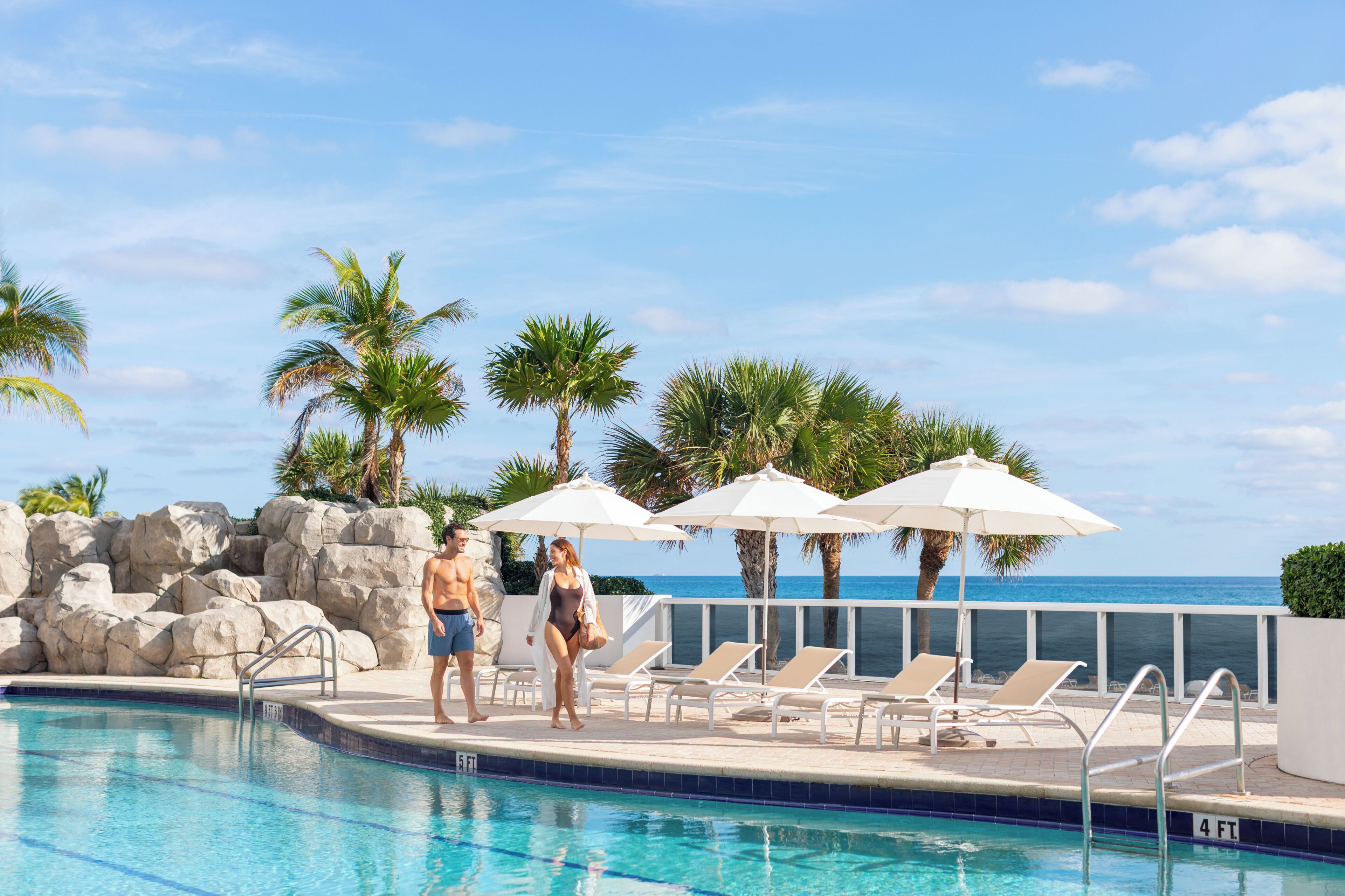 A pool area with lounge chairs and umbrellas, a clear sky, and a rocky wall.