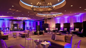 Un espacio lounge moderno con alfombra estampada, sofás de cuero, sillas traslúcidas y un candelabro central.
