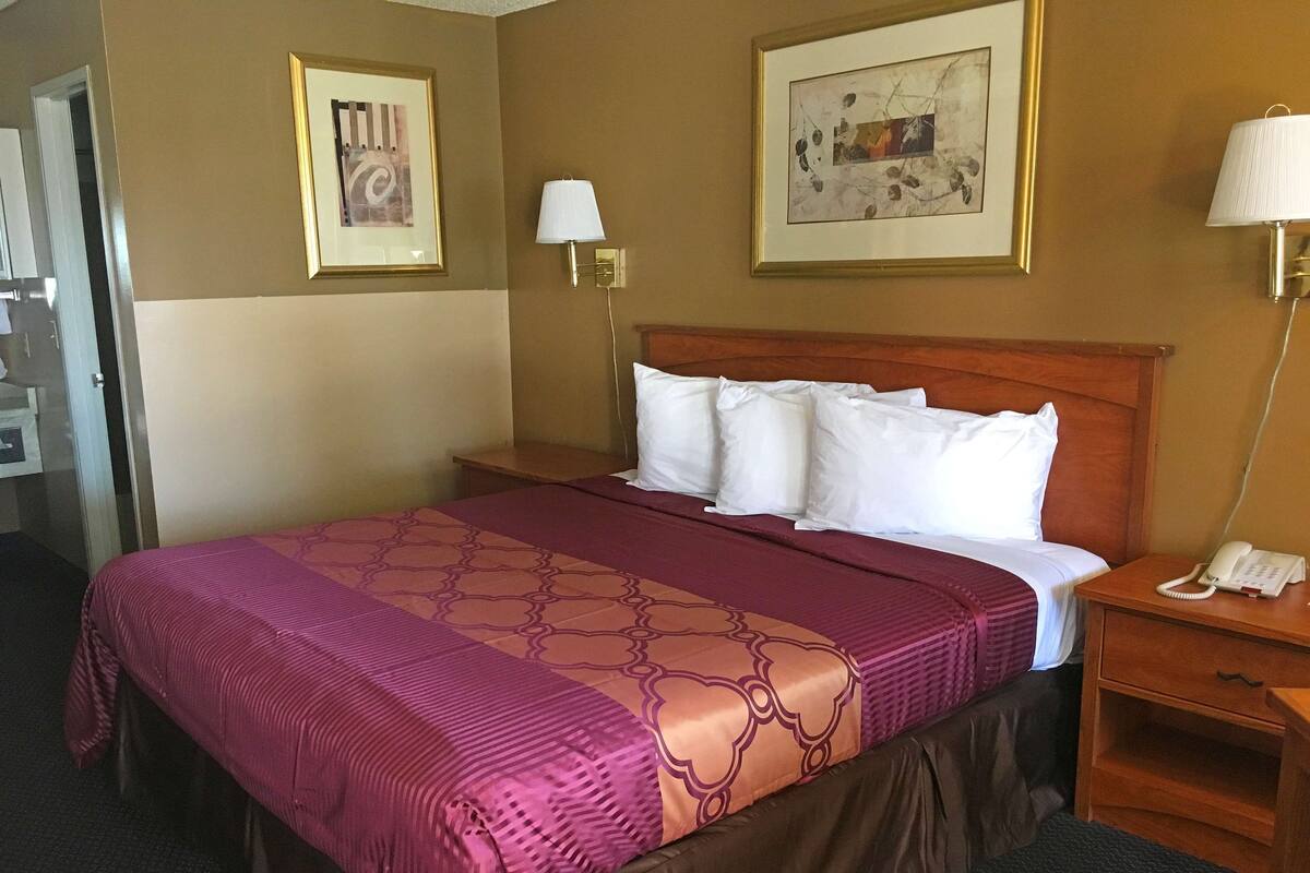 A hotel room with a large bed, a wooden headboard, two wall-mounted lamps, a bedside telephone, and two framed pictures on the walls.