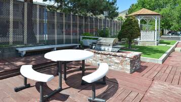 Un patio al aire libre con una parrilla, bancos y un pabellón.