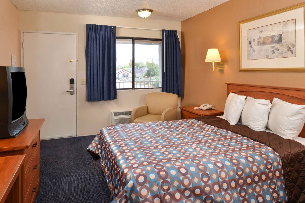 A hotel room with a bed, a chair, a desk, a television, and a window with curtains.
