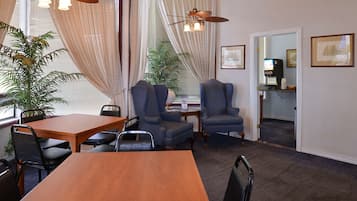 A conference room with a wooden table, four chairs, a potted plant, and a ceiling fan.