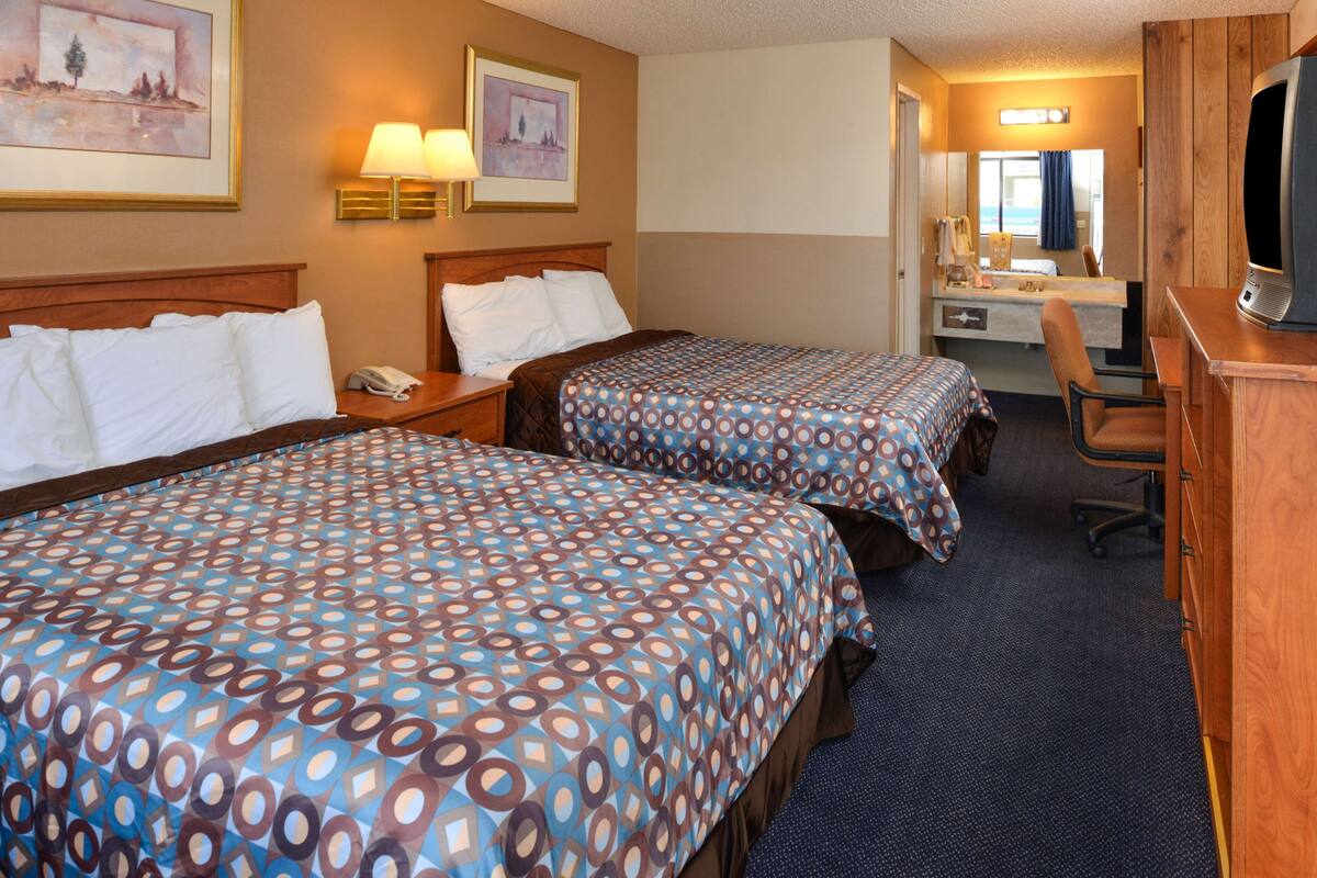 A hotel room with two beds, a desk, a chair, a TV, and a bathroom visible through a door.