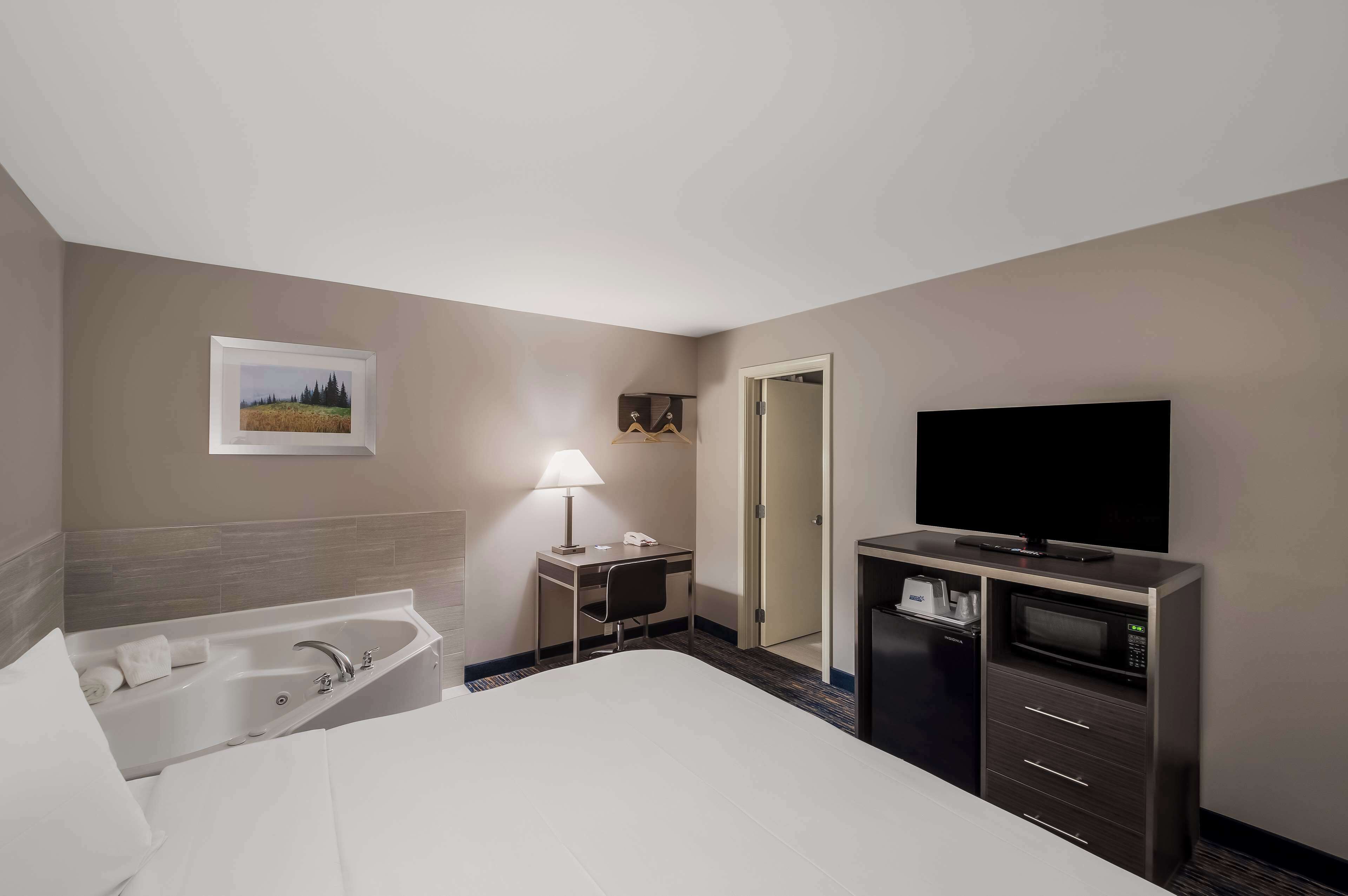 Una habitación de hotel con una cama grande, un escritorio con lámpara, televisión, minibar y baño con bañera.