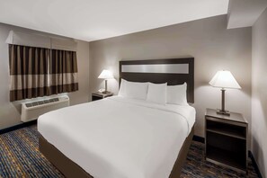 A hotel room with a large bed, two bedside tables with lamps, a window with curtains, and an air conditioning unit. - Americas Best Value Inn Farmington (Farmington)