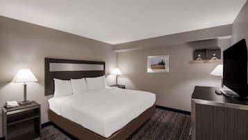 A hotel room with a large bed, two bedside lamps, a desk with a television, and a small picture on the wall.