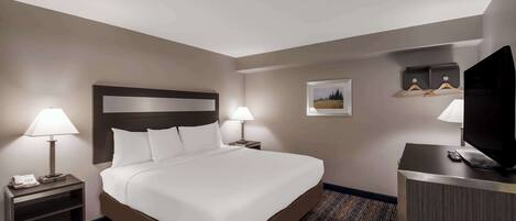 A hotel room with a large bed, two bedside lamps, a desk with a television, and a small picture on the wall.