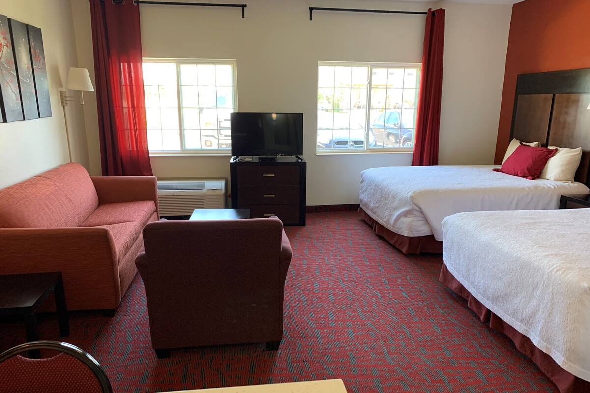 Een hotelkamer met een bank, twee eenpersoonsbedden, een televisie, een bureau en een stoel.