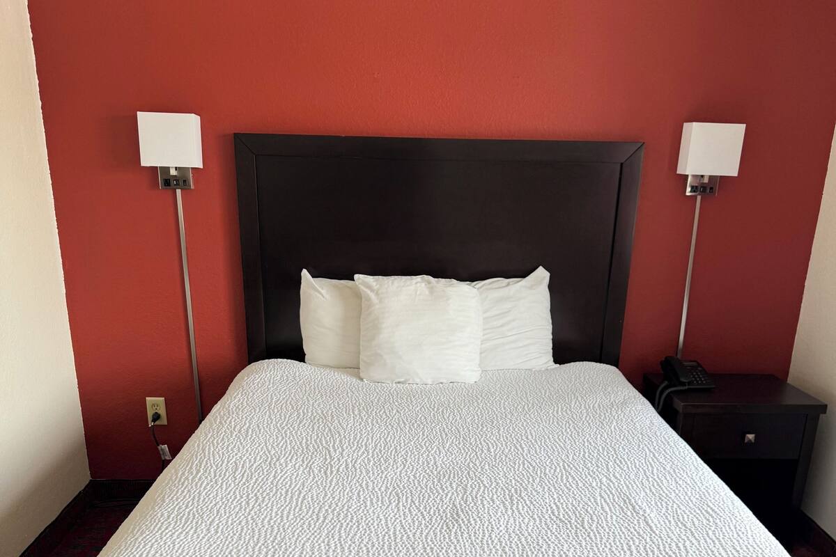 Een hotelkamer met een groot bed, een donker hoofdeinde, twee bedlampjes en een nachtkastje met een telefoon.