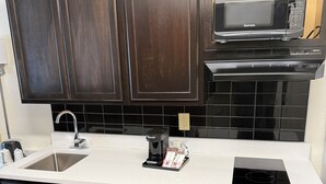 Een moderne keuken met donkere houten kastjes, een wit aanrecht, een roestvrijstalen spoelbak, een koffiezetapparaat, een magnetron en een zwart inductiekookplaatje.