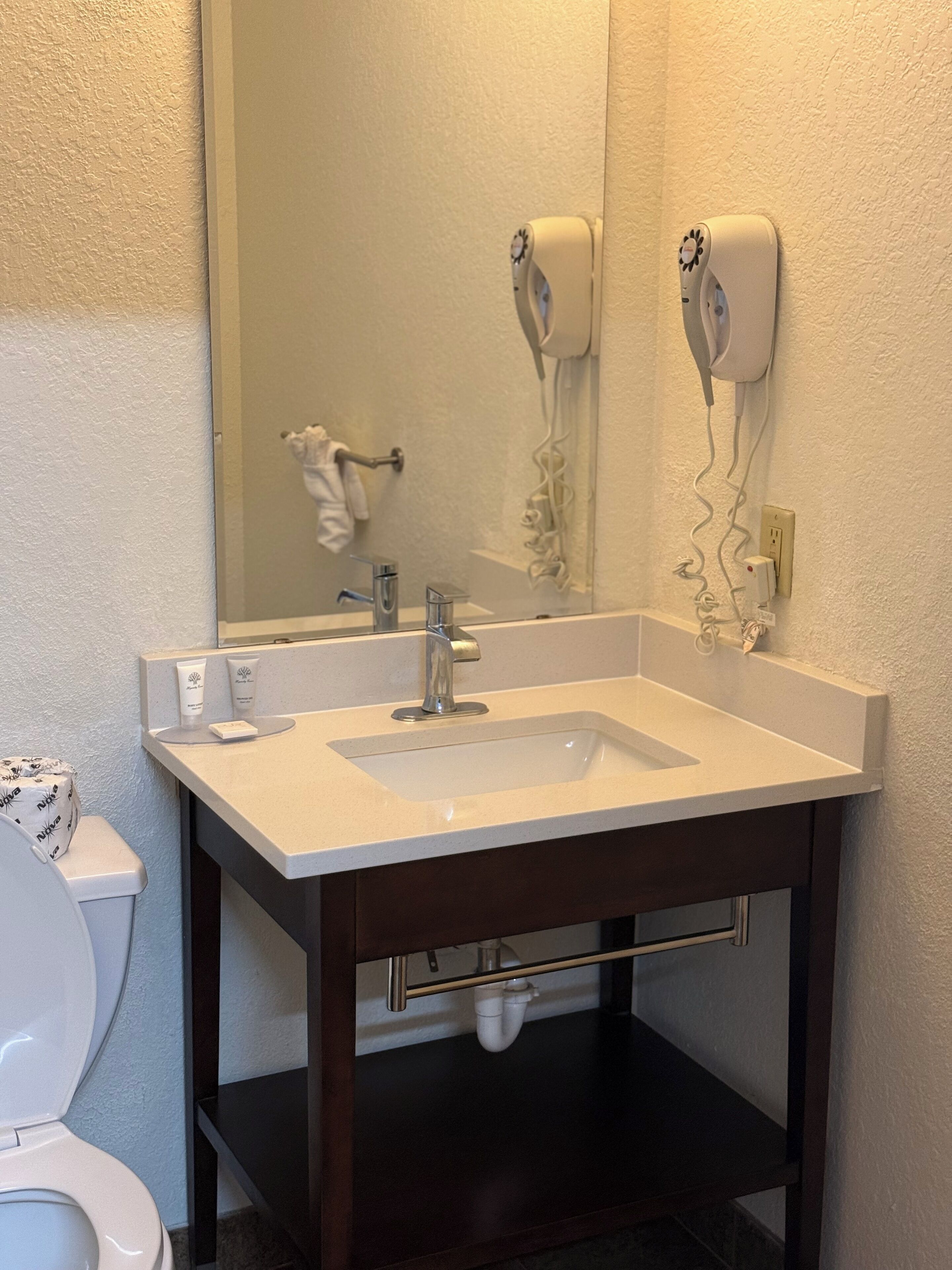 A bathroom with a white sink, dark wooden vanity, a mirror, and a hair dryer mounted on the wall.