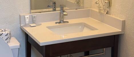 A bathroom with a white sink, dark wooden vanity, a mirror, and a hair dryer mounted on the wall.
