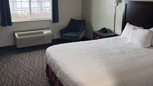 Een hotelkamer met een groot bed, een stoel, een bureau met een lamp en een raam met gordijnen.
