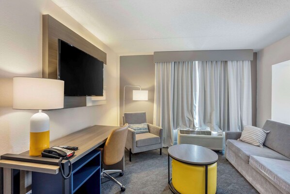 A hotel room with a desk, chair, sofa, and a television.