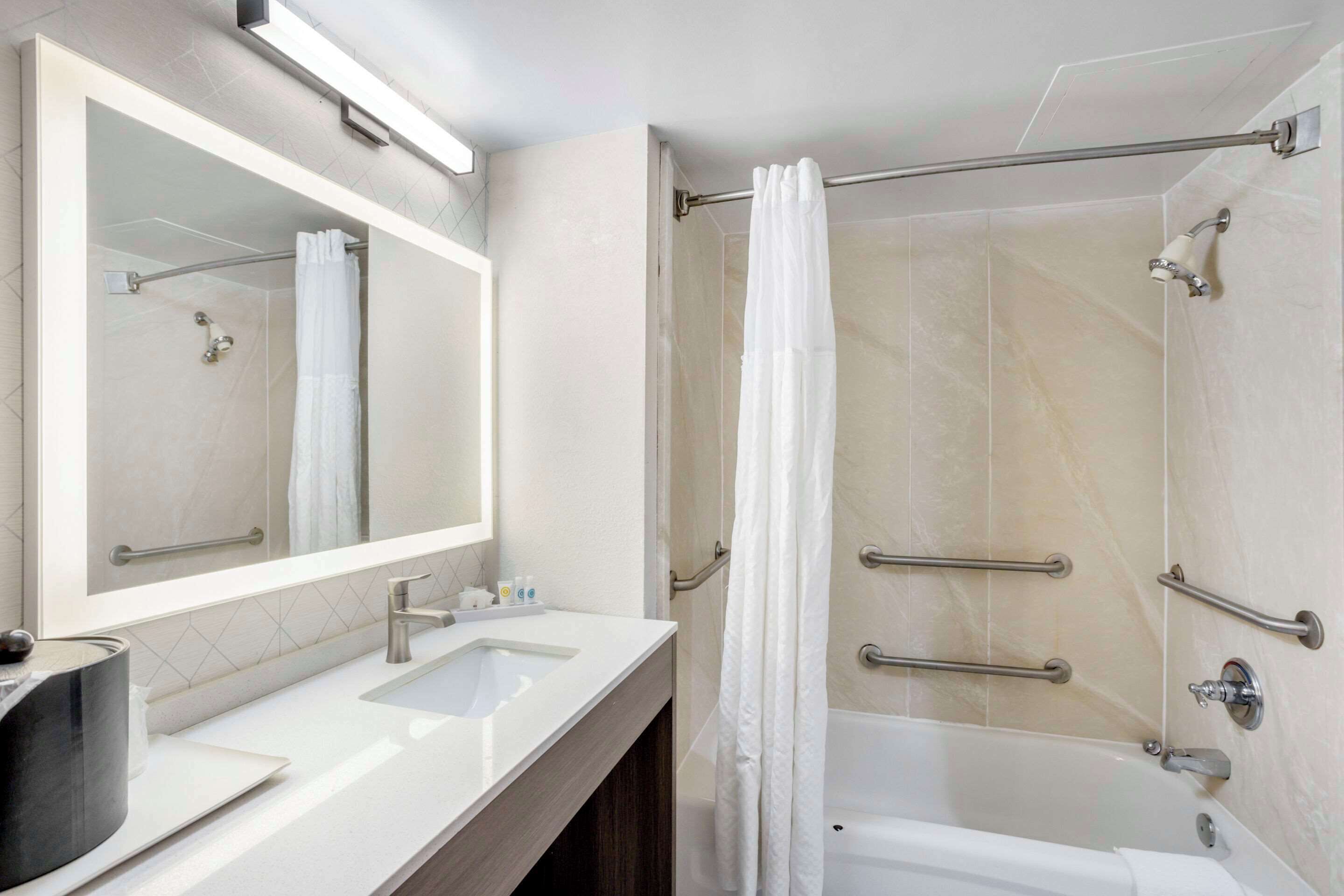A modern bathroom with a large mirror, two sinks, a shower with a glass door, and a bathtub.