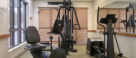 A gym with exercise equipment, a large mirror, and windows with blinds.