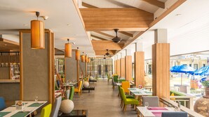Ein Restaurant mit einer langen Theke, mehreren Tischen und Stühlen. Es gibt Pendelleuchten und einen Deckenventilator.