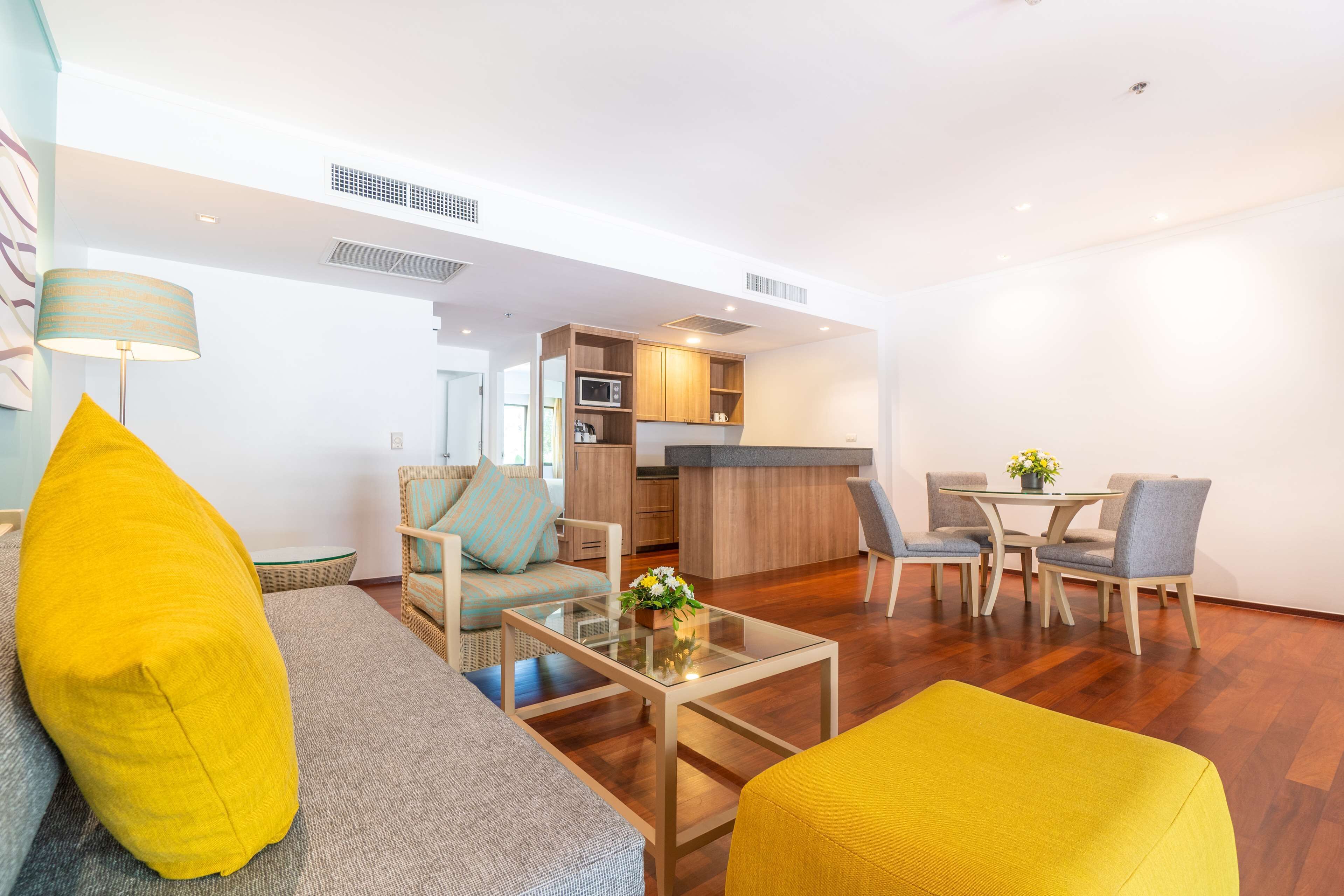 Una sala moderna con un sofá, un sillón y un reposapiés, una mesa de centro de vidrio, y un comedor con sillas y una mesa.