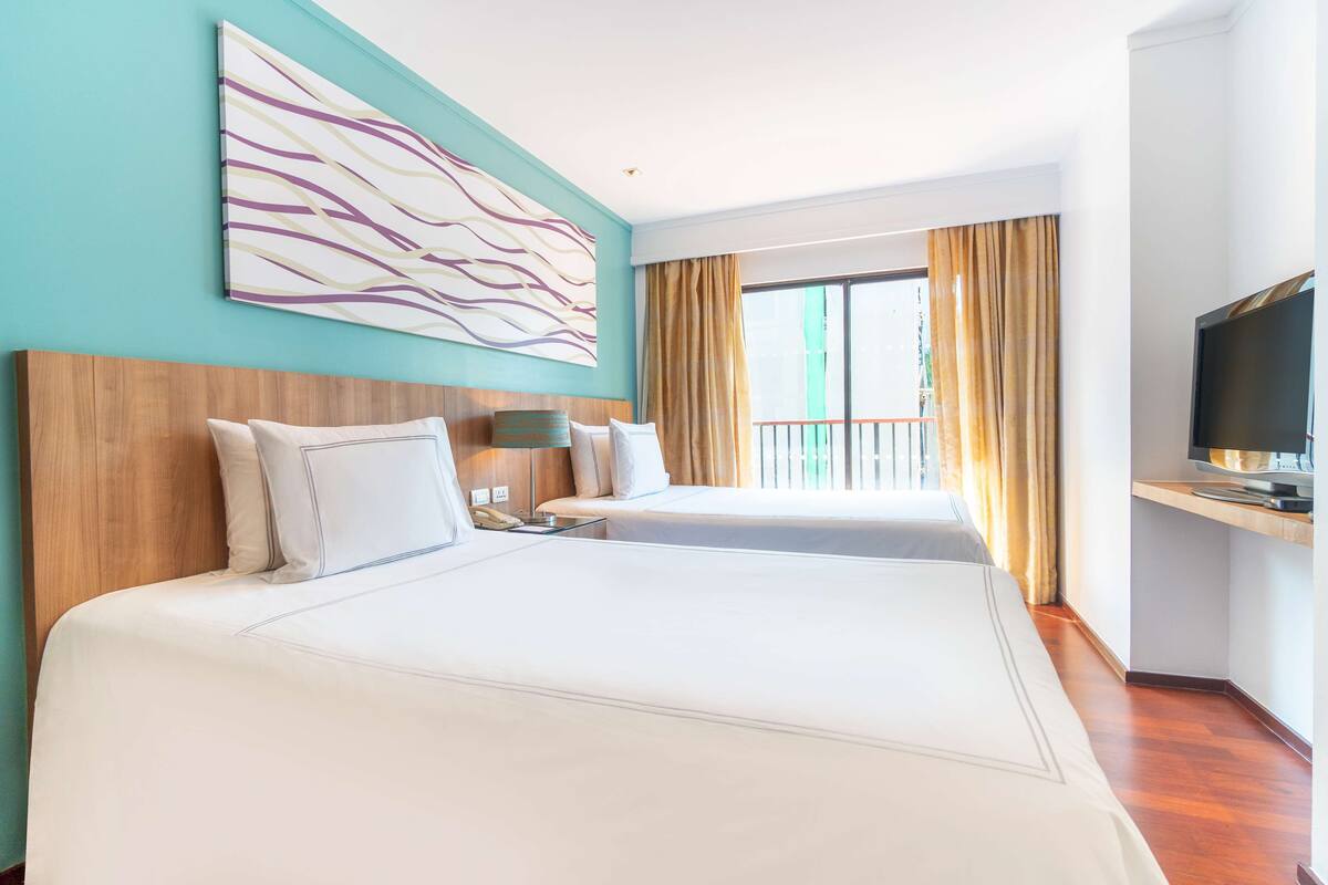 Une chambre d’hôtel avec deux lits, une grande peinture abstraite, un téléviseur et un balcon avec des rideaux.