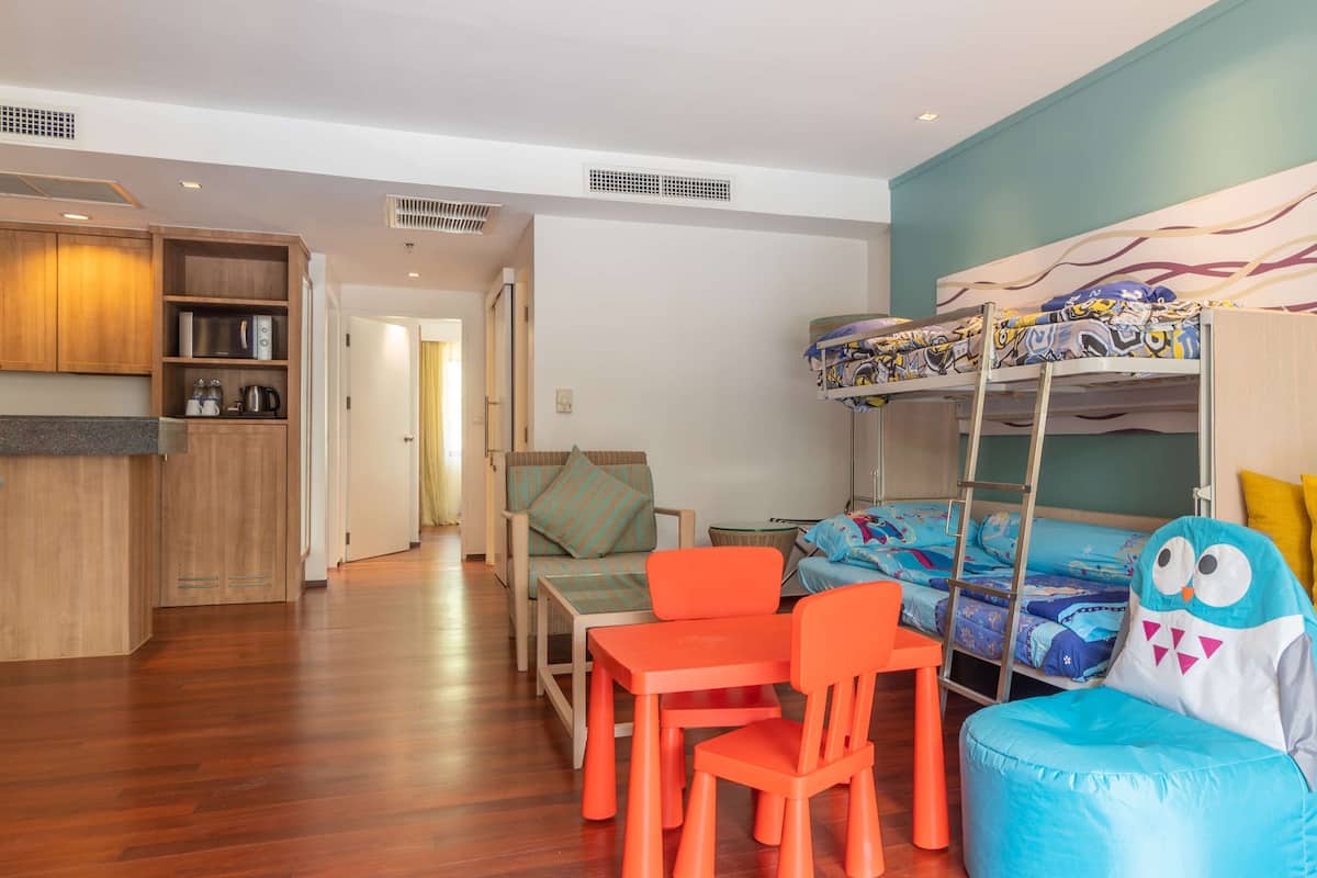 Une pièce compacte comprenant un lit superposé, un petit coin cuisine et un espace salon avec des chaises et une table.