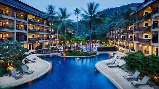 Ein Hotel mit mehreren Stockwerken, einem zentral gelegenen Swimmingpool und Palmen.
