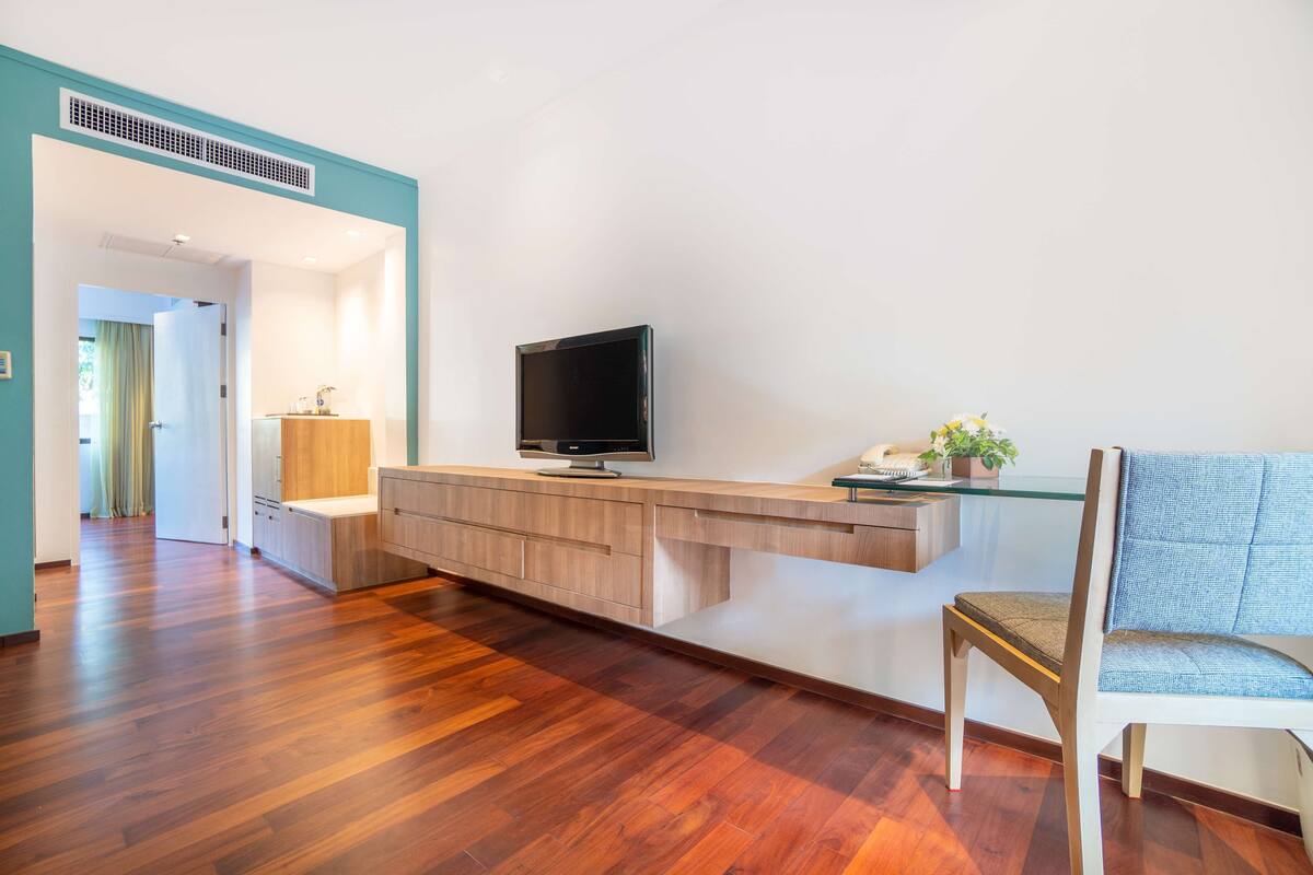 Un salon moderne avec un plancher en bois, un téléviseur fixé au mur, une table basse en verre et un fauteuil bleu.