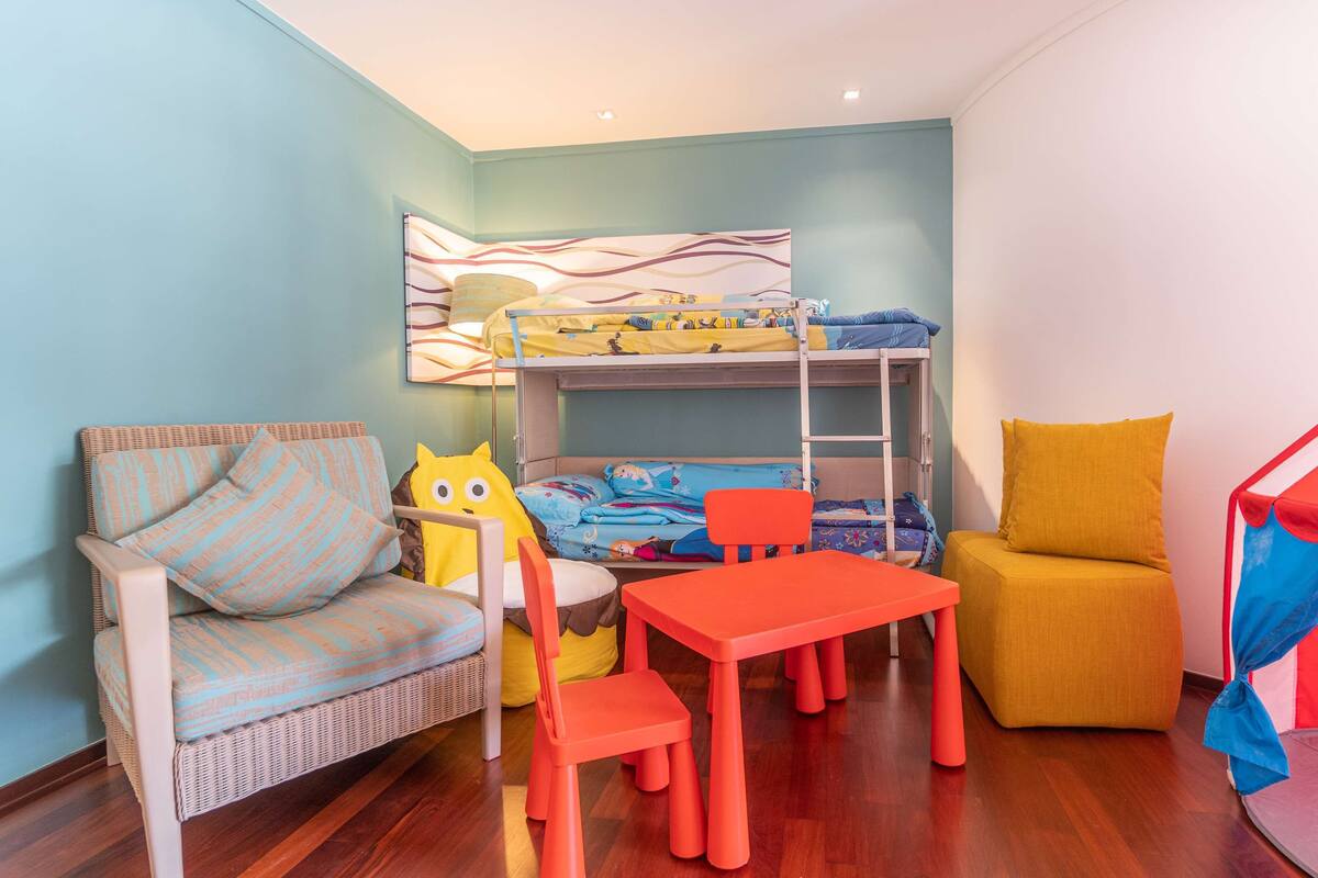 Une chambre d’enfant avec des lits superposés, un fauteuil en osier, une petite table et une tente de jeu.