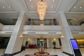 A multi-level hotel lobby with a grand chandelier, a reception desk, and a digital information board. - Luxemon Hotel（Pudong Shanghai） (Shanghai)