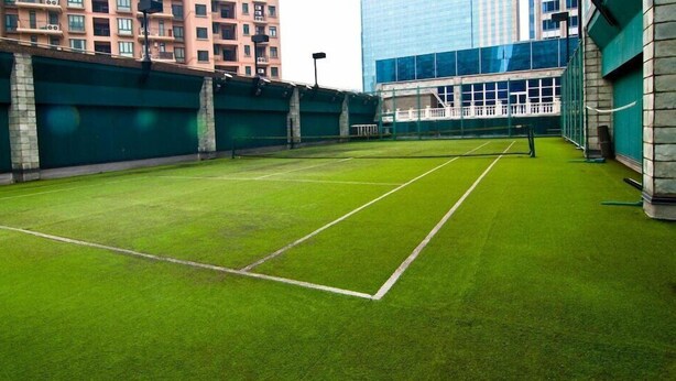 Een tennisbaan met een groene ondergrond, omringd door gebouwen.