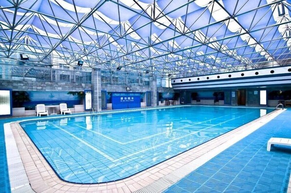 Une piscine intérieure dotée d’un toit en verre, d’une eau cristalline et d’un sol carrelé.