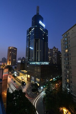 A high-rise building with illuminated signage, surrounded by other buildings and a busy street at dusk. - Luxemon Hotel（Pudong Shanghai） (Shanghai)