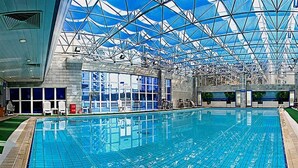 Une piscine intérieure dotée d’un toit en verre, d’une eau d’un bleu cristallin et offrant une vue sur le ciel.