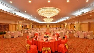 A banquet hall with round tables, chairs, and a large chandelier.