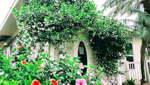 A building with a white exterior, an arched entrance, and a lush garden with various plants and flowers. - Sanibel Siesta on the Beach (Sanibel)