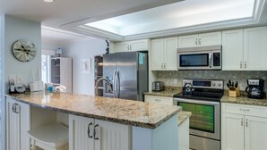 A modern kitchen with white cabinets, stainless steel appliances, granite countertops, and a skylight. - Sanibel Siesta on the Beach (Sanibel)