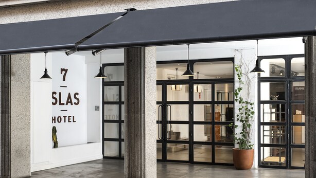 The entrance of the 7-Slas Hotel with a modern design, featuring large glass doors and a potted plant.