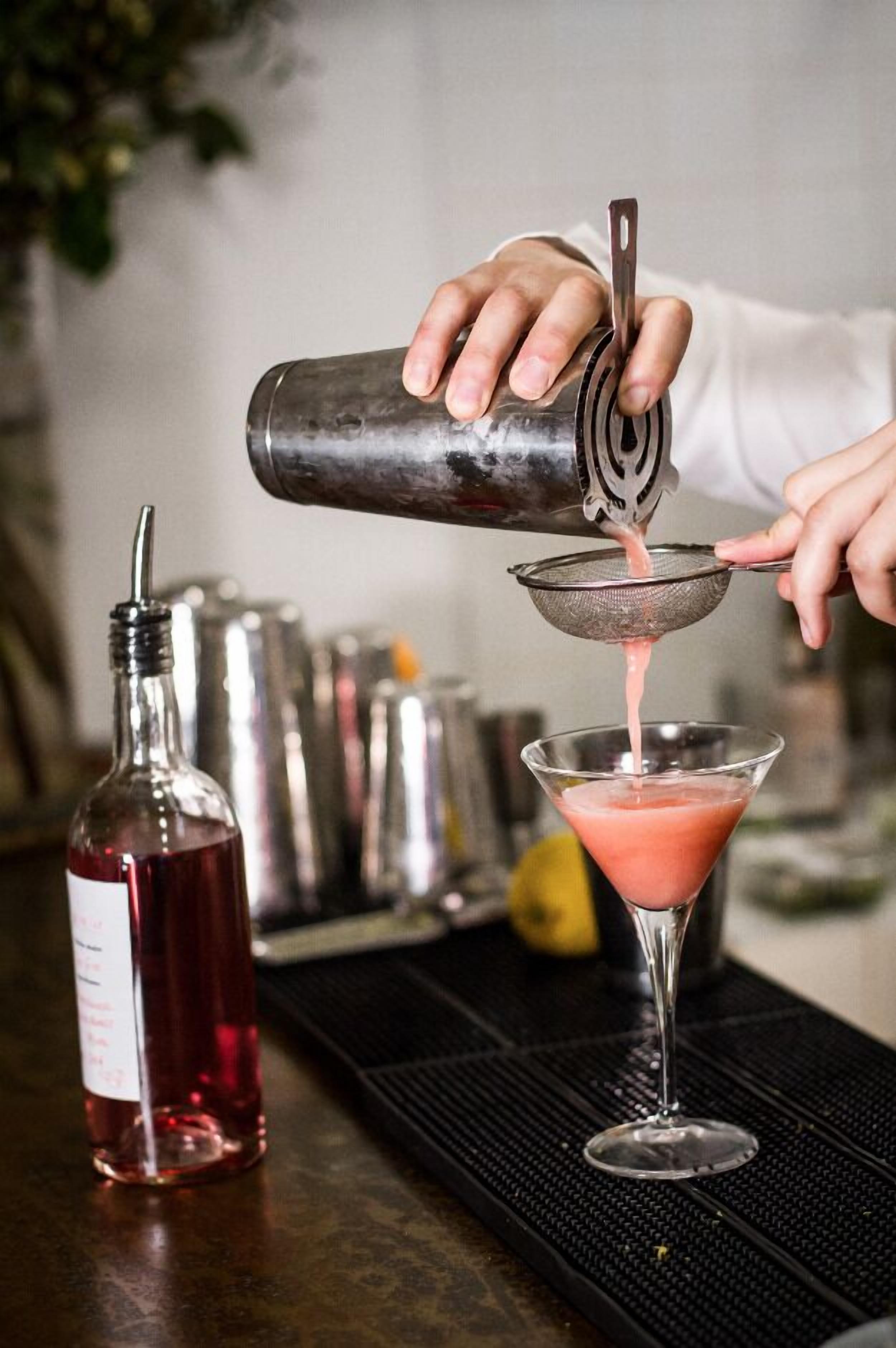 Ein Barkeeper gießt eine rosa Flüssigkeit durch ein Sieb in ein Martini-Glas.