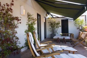 A patio with wooden lounge chairs, a table, and potted plants.