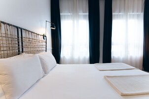 Ein ordentlich bezogenes Bett mit weißen Leinen, ein Kopfteil mit gewebtem Muster und eine Nachttischlampe.